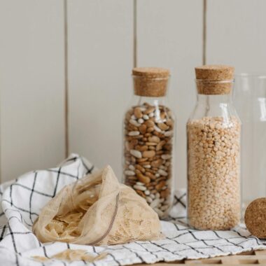 Eco-friendly jars filled with beans and grains, featuring a mesh bag and cloth on a wooden surface.