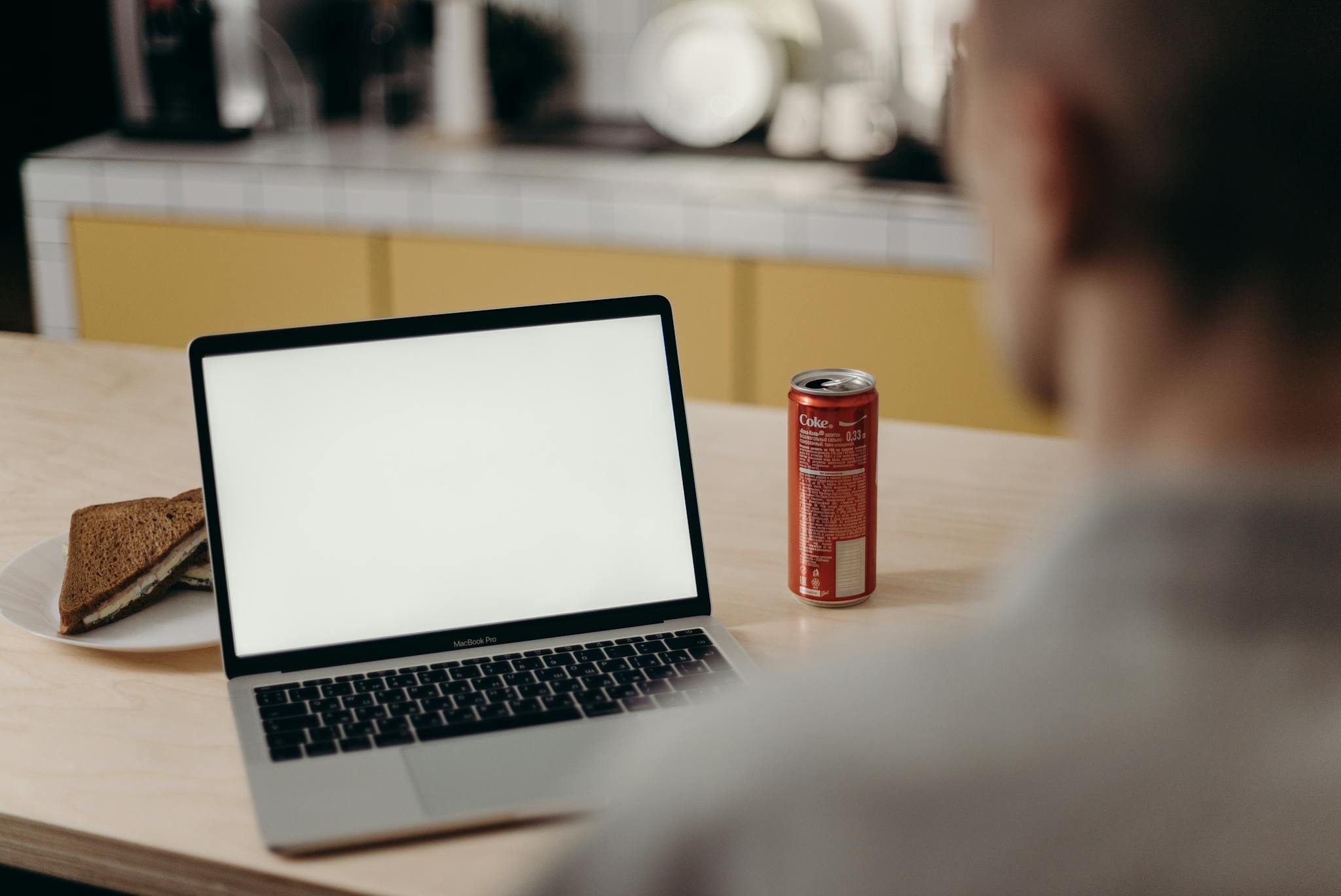 Man at home office desk with blank laptop screen, sandwich, and soda.
