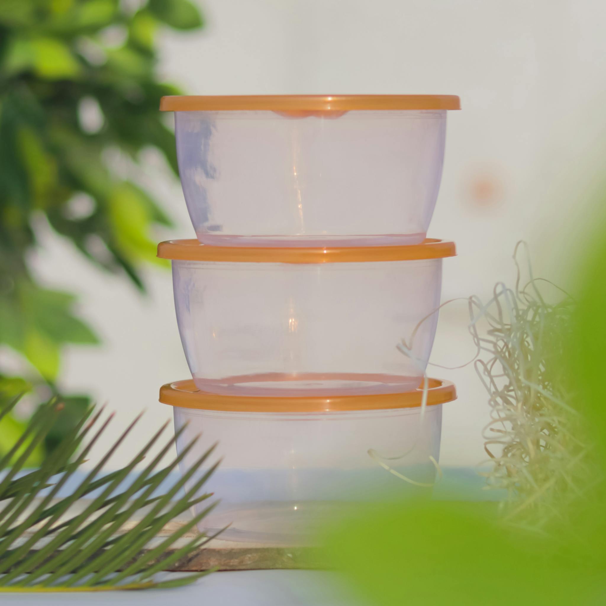 Stacked plastic containers with orange lids amidst greenery, perfect for outdoor storage concepts.